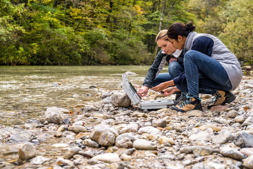 Two women working beside stream collecting samples.