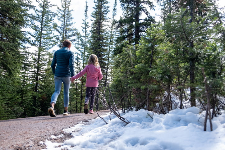 Mother walks with her daughter through a forest with snow on the pathways. Top tourist attractions while visiting the Banff National Park