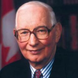 Headshot of man wearing glasses with Canadian flag in the background.